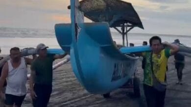 Ketut Arsana Yasa ( kaos putih) ikut menggotong perahu nelayan dibawa ke daratan yang lebih tinggi