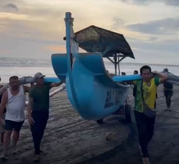 Ketut Arsana Yasa ( kaos putih) ikut menggotong perahu nelayan dibawa ke daratan yang lebih tinggi